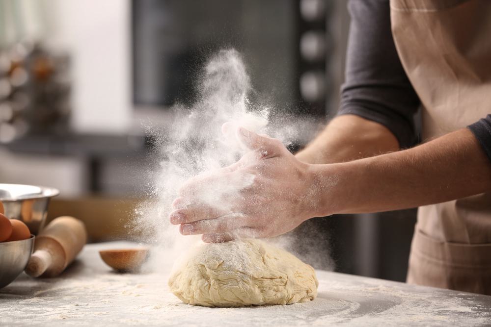 person kneading dough with flour