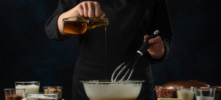 Female chef pours oil into glass bowl with cake batter