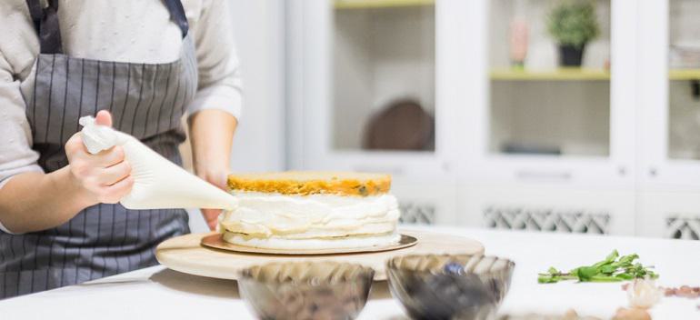 Confectioner with pastry bag squeezing cream on cake at kitchen