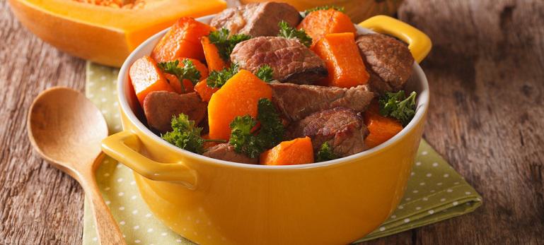 Braised beef with pumpkin, onion and spices close up in a yellow ceramic pan on the table