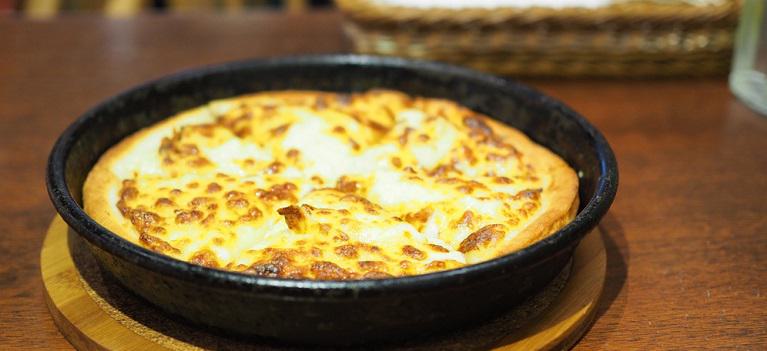 Hot Durian meat Pizza in carbon steel pizza pan on the wood pad and wooden table in restaurant