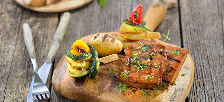 Vegetarian grill platter with vegan seitan slices, courgette rolls with peppers and grilled potato, ciabatta bread in the background