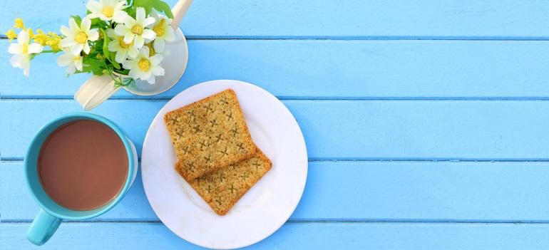 blue cup of hot chocolate and cracker bread on white dish on blue wooden table with white fake flower in white watering