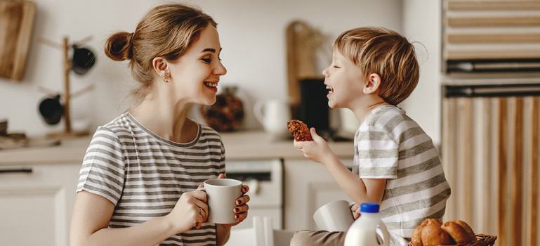 mother and child son cut bread and eat cookies with milk in morning