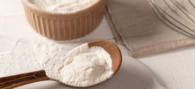 xanthan gum food additive for dough on white plate in wooden spoon with metal whisk