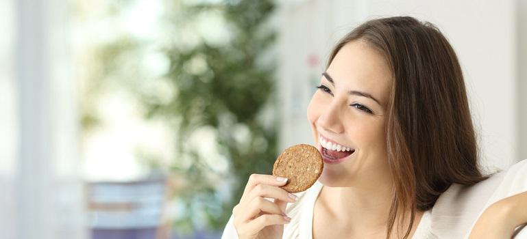 Happy girl eating a cassava cookie sitting on a couch at home