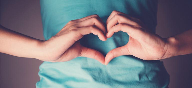 Woman hands making a heart shape on her stomach