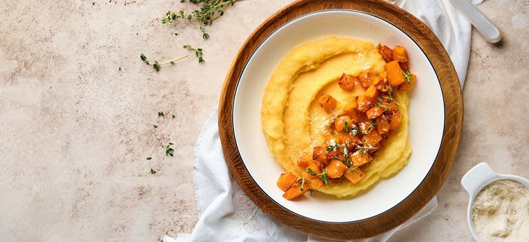 Polenta with butter, pumpkin, garlic, savory and parmesan cheese in white bowl on light concrete background