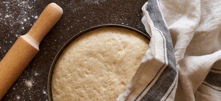 Raw yeast dough resting and rising in large metal bowl covering with linen towel