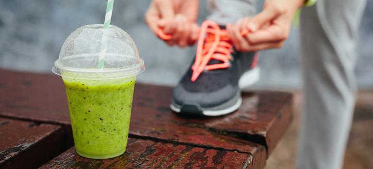 Green protein shake cup and woman lacing running shoes before workout