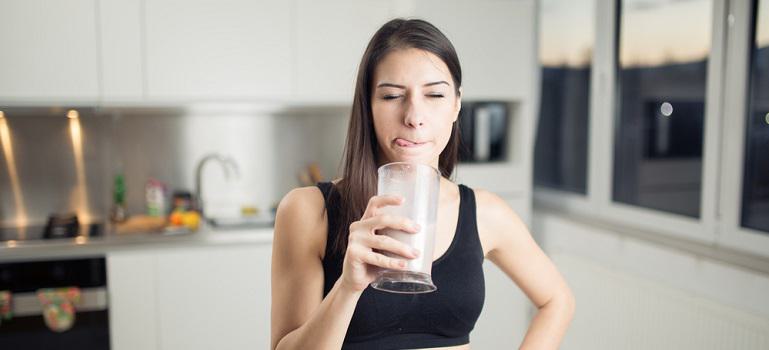 Woman in sportswear drinking whey banana chocolate protein powder smoothie